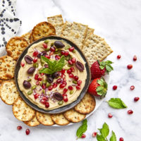 This Mediterranean Hummus Bowl is garnished with Mediterranean Hummus Bowl, toasted pepitas, arils, red onions, and a kiss of mint for a tasty vegetarian snack or lunch!