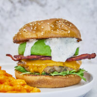 Say hello to your new favorite burger! Ground bacon & seasonings are mixed with ground chicken to make this the ultimate grilled burger! Top with melted cheese, arugula, crispy bacon, and parmesan ranch for absolute deliciousness! Ultimate Ground Chicken Bacon Ranch Burger, crack chicken burger, ground bacon burger, ranch chicken burgers, ultimate chicken burger, best chicken burger