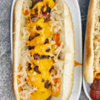 When it comes to the best summer hot dog, these grilled bacon-wrapped cheese and sauerkraut stuffed hot dogs are the best bite of the summer! Ultimate Summer Hot Dogs - Grilled Bacon Wrapped & Stuffed, cheese stuffed hot dogs, bacon wrapped hot dogs, sauerkraut hot dogs, grilled hot dogs