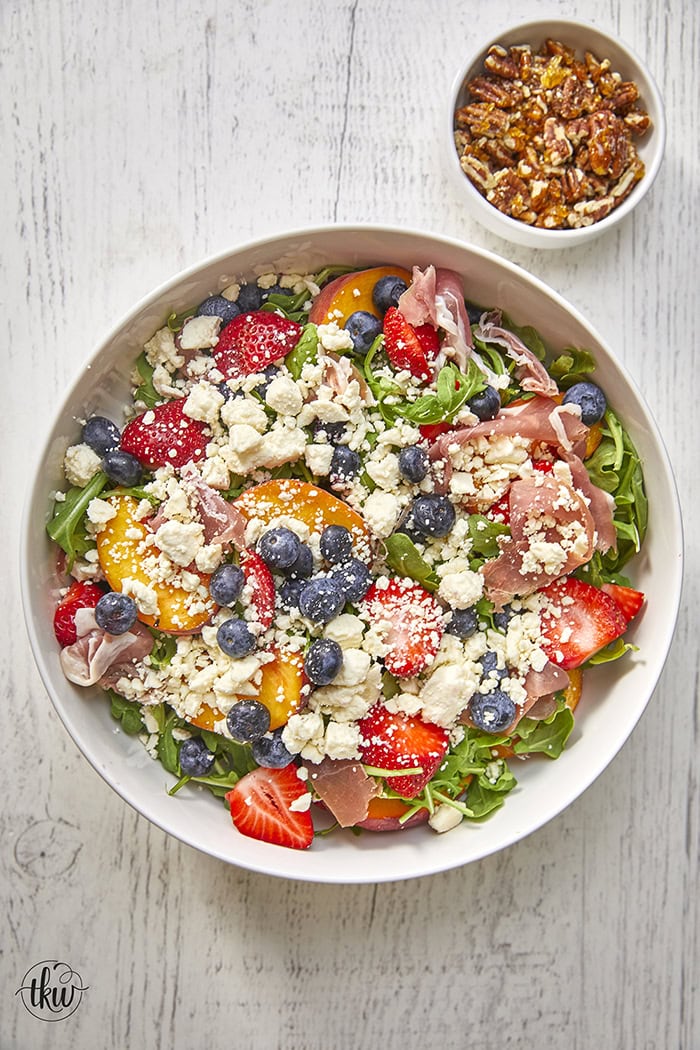 This arugula salad is bursting with freshness from feta, berries, and peaches, drizzled with a maple Dijon vinaigrette, and topped off with crunchy candied nuts. This salad is a delightful blend of savory and sweet that will tantalize your taste buds.