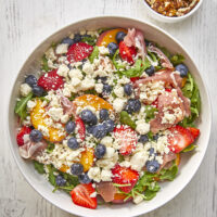 This arugula salad is bursting with freshness from feta, berries, and peaches, drizzled with a maple Dijon vinaigrette, and topped off with crunchy candied nuts. This salad is a delightful blend of savory and sweet that will tantalize your taste buds.