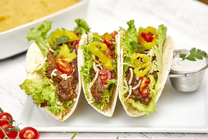 Warm flour tortillas filled with melt-in-your-mouth beef infused with bold spices, tangy banana peppers, fresh veggies, lime crema, and a sprinkling of cheese make these tacos a standout at any dinner table.