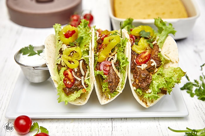 Warm flour tortillas filled with melt-in-your-mouth beef infused with bold spices, tangy banana peppers, fresh veggies, lime crema, and a sprinkling of cheese make these tacos a standout at any dinner table.