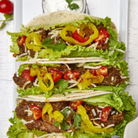 Warm flour tortillas filled with melt-in-your-mouth beef infused with bold spices, tangy banana peppers, fresh veggies, lime crema, and a sprinkling of cheese make these tacos a standout at any dinner table.