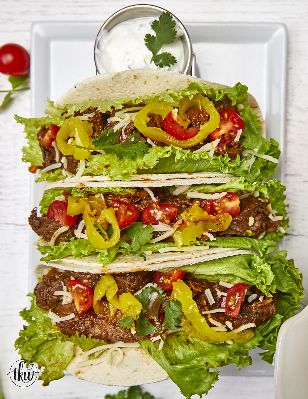 Warm flour tortillas filled with melt-in-your-mouth beef infused with bold spices, tangy banana peppers, fresh veggies, lime crema, and a sprinkling of cheese make these tacos a standout at any dinner table.