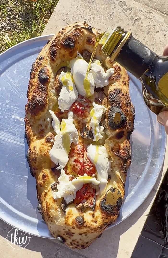 This wood-fired pizza, shaped like khachapuri, has a cheesy crust stuffed with cremini mushrooms, crispy bacon, and datterini tomatoes. It's then kissed with olive oil and finished with burrata, making it your new favorite pizza!